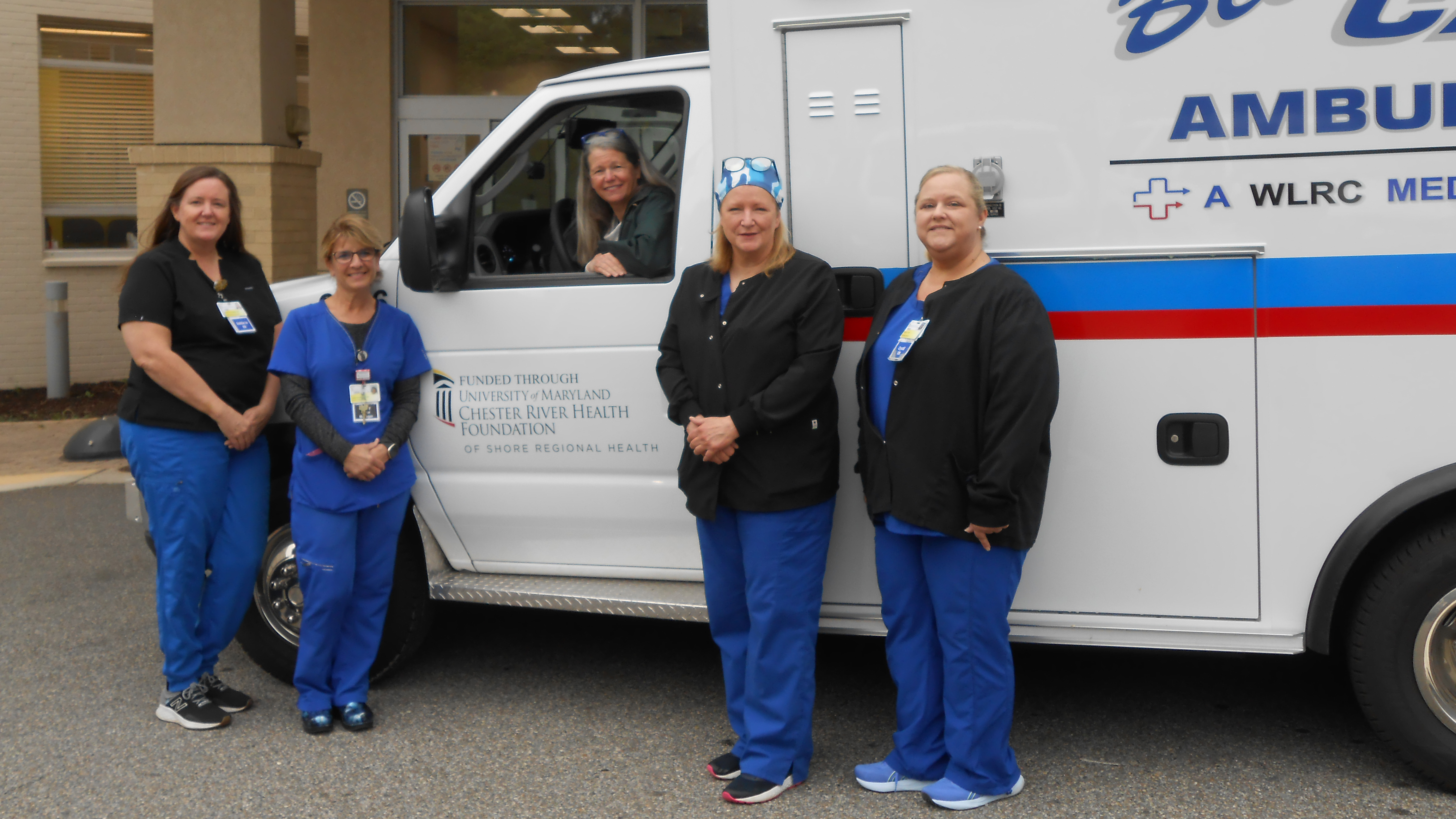 Four nurses stand in front of an ambulance while the chairperson of the Chester River Health Foundation sits in the driver's seat of the ambulance.