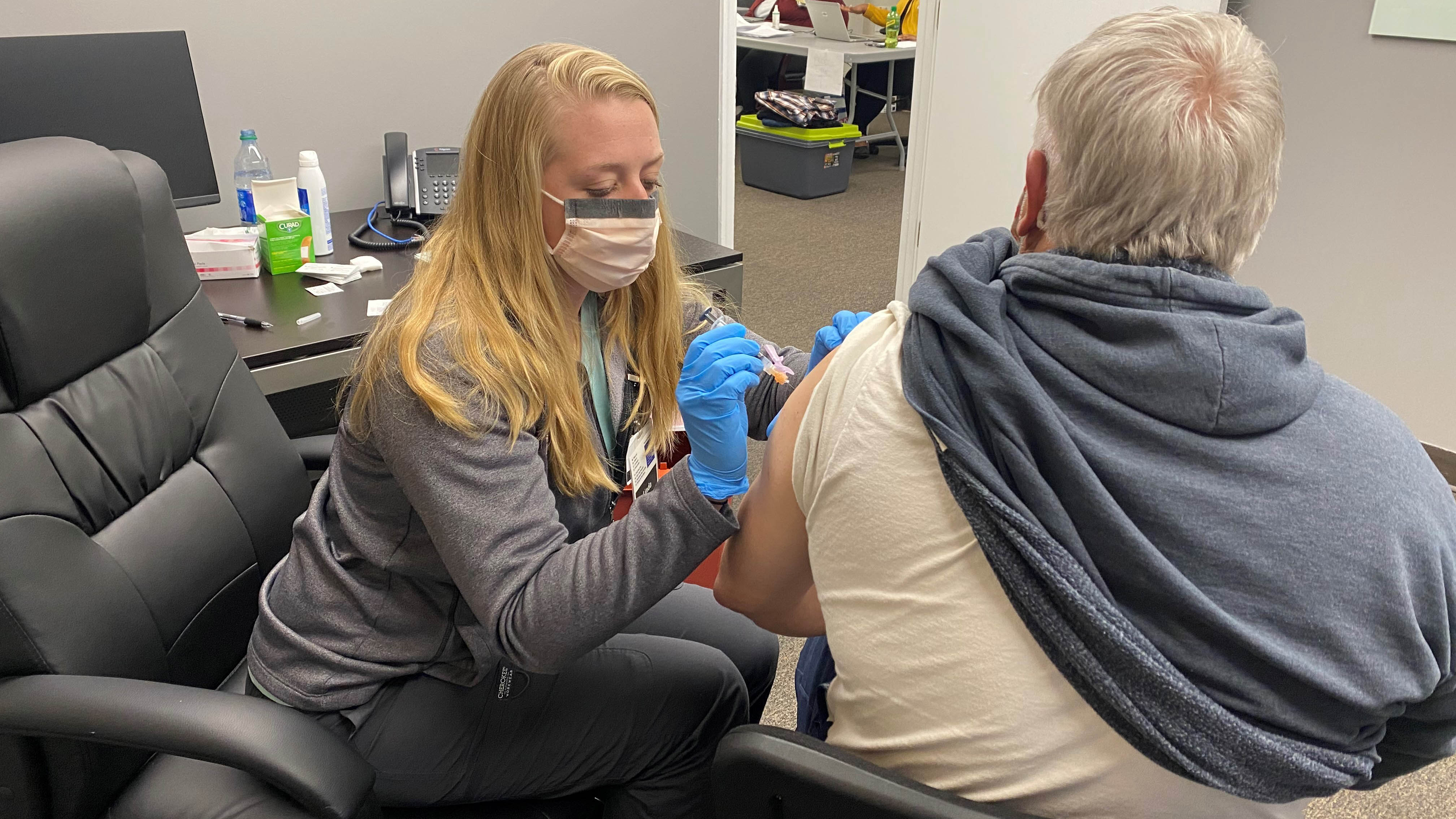 A female pharmacy employee vaccinates a patient with the COVID-19 vaccine.